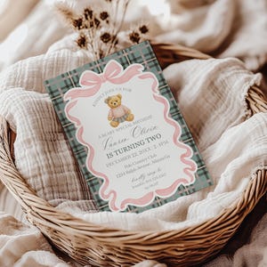 May include: A birthday invitation card with a teddy bear illustration, set in a woven basket. The card features a pink ribbon and text that reads "Lauren Olivia is turning two." The background has a plaid pattern in teal and white.