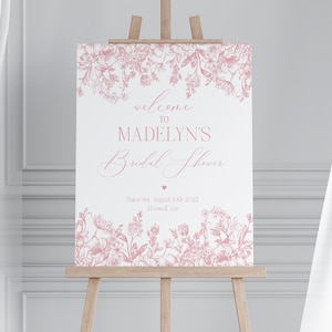 May include: A pink floral bridal shower welcome sign with the text "Welcome to Madelyn's Bridal Shower" and the date "Saturday, August 10th, 2022".