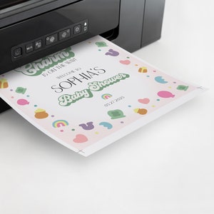 May include: A pink baby shower invitation with green, yellow, and blue accents. The invitation says "Charm is oh the rush! Welcome to Sophia's Baby Shower 03.27.2025".
