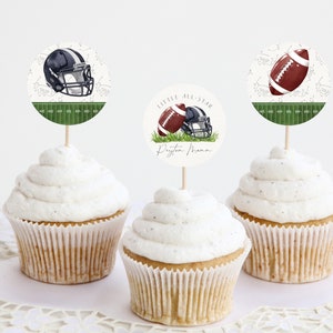 May include: Three cupcakes with white frosting topped with round paper cupcake toppers featuring a football helmet, a football, and a football helmet and football with the text "Little All-Star Dayton Mama".