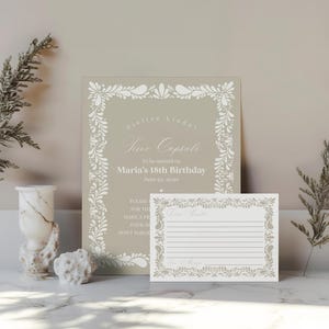 Può includere: Una scheda di capsula del tempo beige e un biglietto di accompagnamento con bordo floreale. La scheda della capsula del tempo recita "Cielito Linda Time Capsule" e "Maria's 18th Birthday". Il biglietto ha delle righe per scrivere. Rametti decorativi e un vaso di marmo sono anche nell'immagine.
