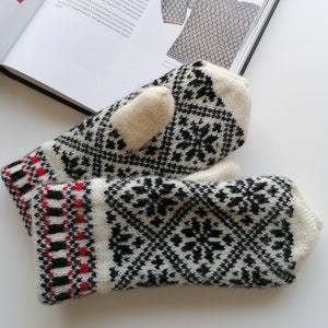 May include: A pair of white and black knitted mittens with a red and black trim. The mittens have a traditional Scandinavian pattern.
