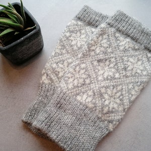 Könnte beinhalten: Graue und weiße gestrickte Fingerlose Handschuhe mit einem Rautenmuster.