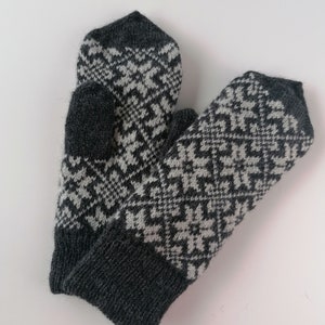 Peut inclure: Une paire de mitaines en tricot gris et blanc avec un motif géométrique. Les mitaines sont pliées ensemble et ont un aspect épais et chaud.