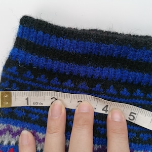 May include: A close-up of a blue and black striped knitted sock with a measuring tape across it. The tape reads "60 in" and shows measurements in inches.