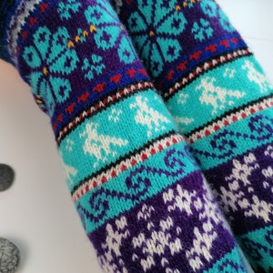 May include: A pair of long, knitted socks with a colorful, geometric pattern. The socks are blue, purple, white, red, and black. The pattern features snowflakes and other abstract designs.