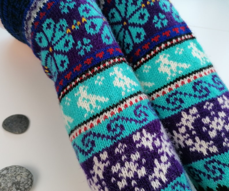 May include: A pair of long, knitted socks with a colorful, geometric pattern. The socks are blue, purple, white, red, and black. The pattern features snowflakes and other abstract designs.