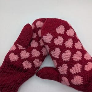Può includere: Un paio di guanti rossi lavorati a maglia con un motivo a cuori rosa. I guanti sono realizzati in un materiale morbido e caldo, perfetto per il freddo. Il motivo a cuore aggiunge un tocco di fascino.