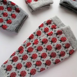 May include: A pair of gray knitted socks with a red ladybug pattern. The socks are folded and displayed on a white surface.