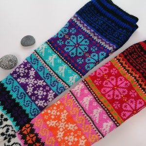 May include: Two pairs of colorful knitted leg warmers with intricate patterns. The leg warmers are made with a variety of colors, including red, orange, yellow, green, blue, purple, and white.