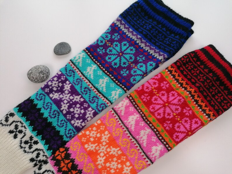 May include: Two pairs of colorful knitted leg warmers with intricate patterns. The leg warmers are made with a variety of colors, including red, orange, yellow, green, blue, purple, and white.