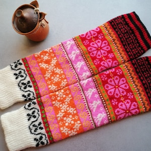 May include: A pair of colorful knitted leg warmers with a white base and a pattern of pink, orange, red, and black. The leg warmers are made with a traditional Scandinavian design.
