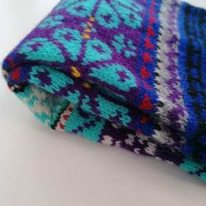 May include: A folded knitted scarf with a colorful geometric pattern in shades of blue, purple, turquoise, white, red, and black.