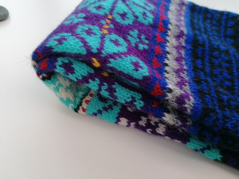 May include: A folded knitted scarf with a colorful geometric pattern in shades of blue, purple, turquoise, white, red, and black.