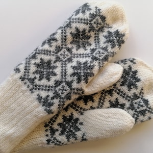 May include: A pair of white knitted mittens with a black and white geometric pattern.