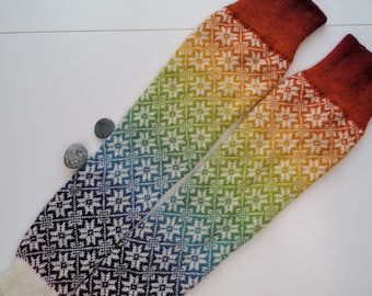 May include: A pair of rainbow knit leg warmers with a white background and a geometric pattern. The leg warmers are folded in half and the top of the leg warmers are a rust color.