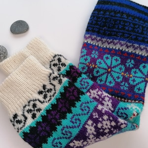 May include: A pair of colorful knitted socks with a white, blue, purple, and turquoise pattern. The socks have a traditional Scandinavian design.