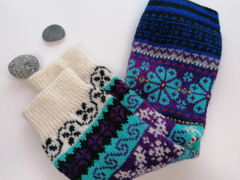 May include: A pair of colorful knitted socks with a white, blue, purple, and turquoise pattern. The socks have a traditional Scandinavian design.