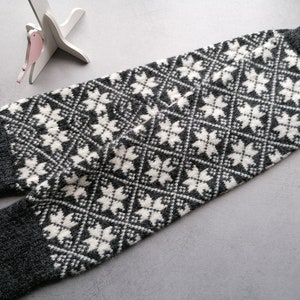 Op de afbeelding: Grijze en witte gebreide beenwarmers met een geometrisch sneeuwvlokkenpatroon.