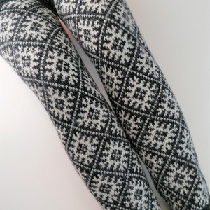 Op de afbeelding: Een paar zwart-witte gebreide beenwarmers met een geometrisch patroon.