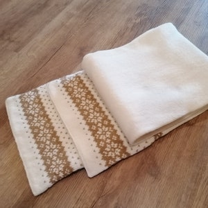 May include: Three white knitted scarves with a brown and white geometric pattern. The scarves are folded and stacked on top of each other.