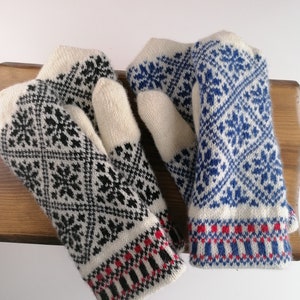 May include: Pair of white knitted mittens with black and blue geometric patterns. The mittens have red and white trim.