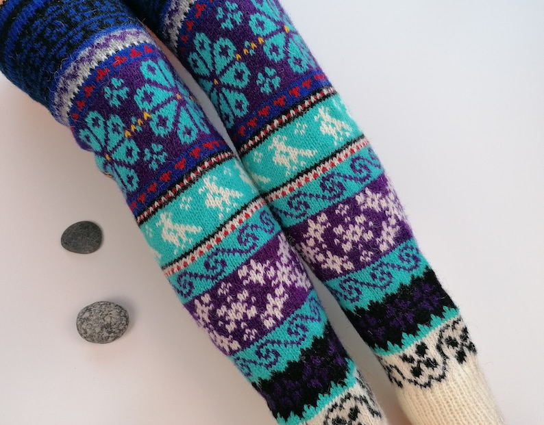 May include: A pair of knitted leg warmers with a colorful geometric pattern in shades of blue, purple, white, and black. The leg warmers have a white cuff at the top.