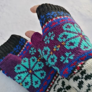 May include: A pair of fingerless gloves with a colourful knit pattern. The gloves are purple, blue, teal, black, white and red. The pattern features a snowflake design.