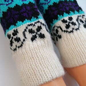 May include: A pair of white knitted leg warmers with a colorful geometric pattern. The pattern features blue, purple, and black colors.