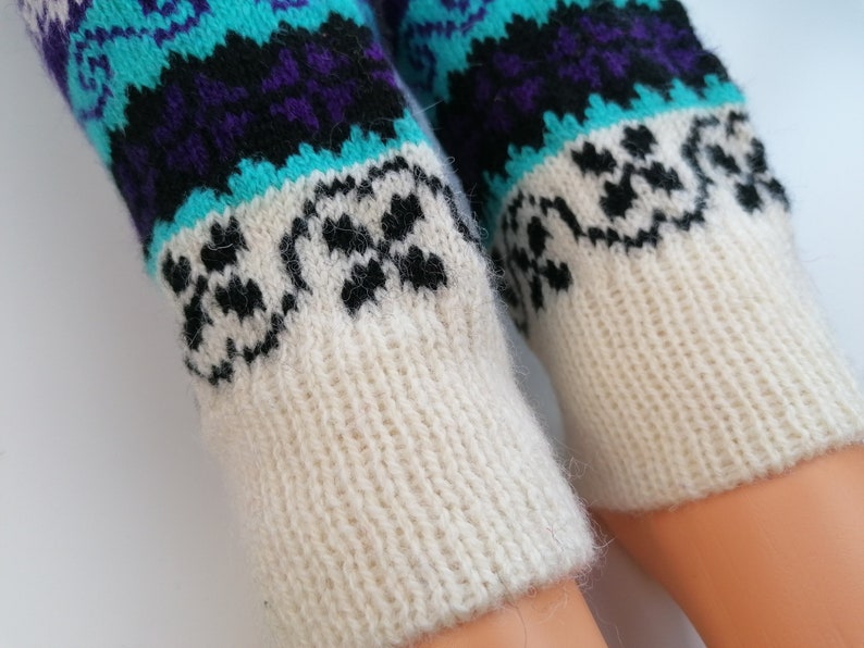 May include: A pair of white knitted leg warmers with a colorful geometric pattern. The pattern features blue, purple, and black colors.