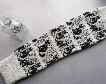 May include: A white knitted leg warmer with a black cat pattern. The leg warmer is made of a soft, cozy material and has a ribbed texture.