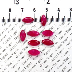 Peut inclure: Neuf pierres précieuses ovales de couleur rose, mesurant chacune environ 1 cm de long, sont disposées sur une surface blanche avec une règle pour l'échelle.