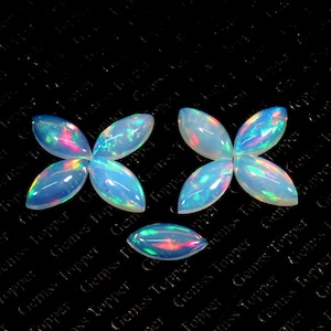 May include: Six iridescent opal cabochons in a teardrop shape with a pointed end. The opals are arranged in a flower pattern with three opals on each side. The opals are a light blue color with flashes of pink, green, and yellow.