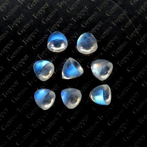 May include: A collection of eight iridescent moonstone cabochons, each with a unique blue sheen. The stones are faceted and have a teardrop shape. They are arranged on a black background.