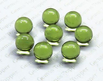 May include: Eight translucent, round, olive-green gemstones are arranged on a white surface. The gems have a smooth, polished appearance, reflecting light. The background has a repeating pattern of text that reads "Gemss Topper".