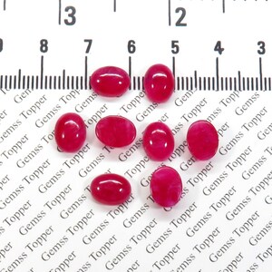 Pode incluir: Oito pedras preciosas ovais de cor rosa, com um leve tom vermelho, são dispostas sobre uma superfície branca com uma régua no fundo. A régua é marcada com números de 1 a 8.