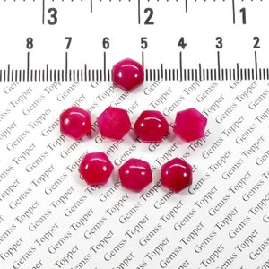 May include: Ten pink hexagonal gemstone beads, each with a slightly different shade of pink. The beads are arranged in a random pattern on a white surface with the text "Gemss Topper" repeated across the surface.