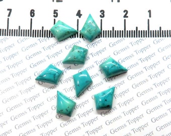 May include: Seven polished turquoise gemstones with irregular kite-like shapes and dark matrix veining, arranged below a ruler showing measurements in inches. The stones exhibit a vibrant blue-green color with smooth, reflective surfaces.