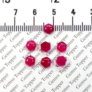 May include: Eight faceted ruby red gemstone beads, each approximately 5mm in diameter, are scattered on a white surface with the text "Gemss Topper" repeated in black.