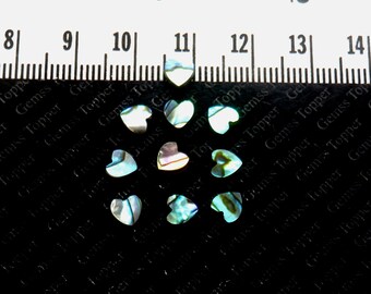 May include: A group of ten iridescent abalone shell heart-shaped embellishments. The hearts are approximately 1 cm in size and have a blue, green, and white color scheme.