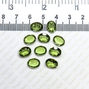 Puede incluir: Diez piedras preciosas verdes de forma ovalada, probablemente peridotos, dispuestas sobre una superficie blanca con una regla en el fondo. La regla está marcada en pulgadas.