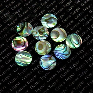 May include: A collection of ten iridescent abalone shell cabochons. The cabochons are round and have a variety of colors, including green, blue, purple, and gold. The cabochons are arranged in a random pattern on a black background.