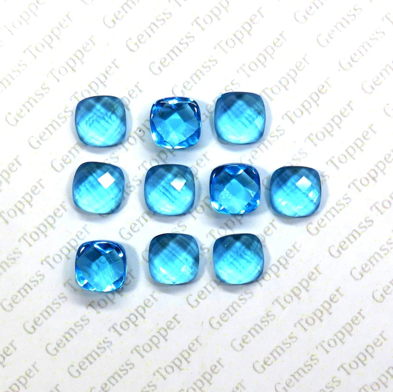 May include: Ten light blue cushion-cut gemstones, each with a faceted surface, are arranged in three rows on a white background.