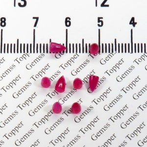May include: A collection of eight pink gemstone cabochons of various shapes and sizes, displayed on a white surface with a ruler marked in inches.