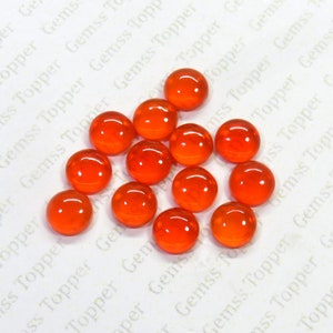 Könnte beinhalten: Eine Ansammlung von runden, polierten orangefarbenen Edelsteinen. Die Edelsteine sind gleichmäßig verteilt und haben eine glänzende, reflektierende Oberfläche. Das Bild ist aus der Vogelperspektive aufgenommen und zeigt die Edelsteine vor einem weißen Hintergrund.