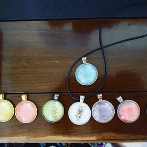 May include: A set of nine round glass pendants with various designs. The pendants are silver with a black cord. The designs include a blue swirl, a yellow swirl, a pink swirl, a green swirl, a white swirl, a purple swirl, a red swirl, a blue skull, and a white design.