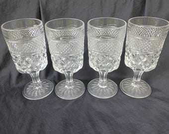 May include: A set of four clear glass goblets featuring a textured diamond pattern on the upper bowl and a faceted stem base. Each glass has a cylindrical shape with a wide rim and a sturdy footed bottom, showcasing a pressed glass design.