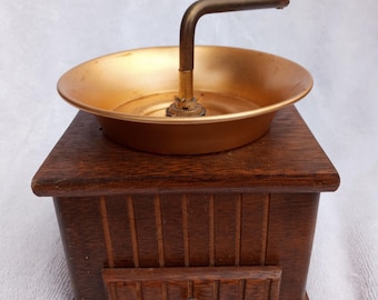 May include: A vintage wooden coffee grinder with a gold-colored metal top and a wooden handle. The grinder has a drawer for collecting the ground coffee.