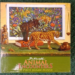 May include: A 750-piece jigsaw puzzle box titled Bo Newell Animal Encounters. The box features a painting of a black panther and a spotted leopard in a jungle setting, with a small figurine, a book, and a frog-shaped object on a table.