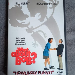 May include: DVD case for the movie "What About Bob?" featuring Bill Murray and Richard Dreyfuss. The cover art includes a cartoon silhouette and a photo of the actors shaking hands. The text "Howlingly Funny!" is displayed.